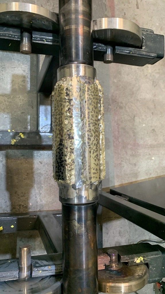 Freshly applied tungsten carbide hardfacing weld beads on shaft before finishing